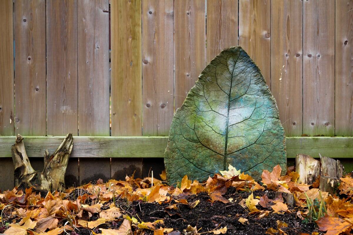 A green stone leaf rests against wood and autumn leaves in Peterborough, Ontario. print option