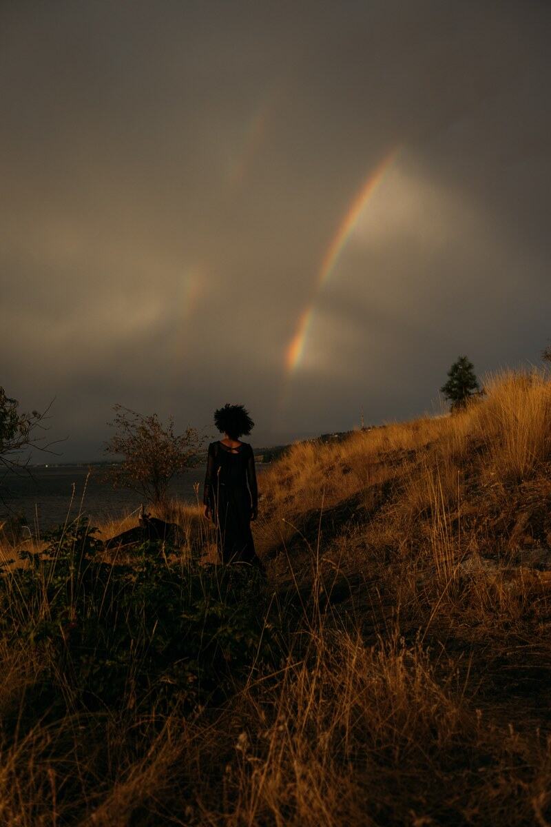 Rebekah stands small on the Okanagan Lake hillside below rainbow and storm light. print option