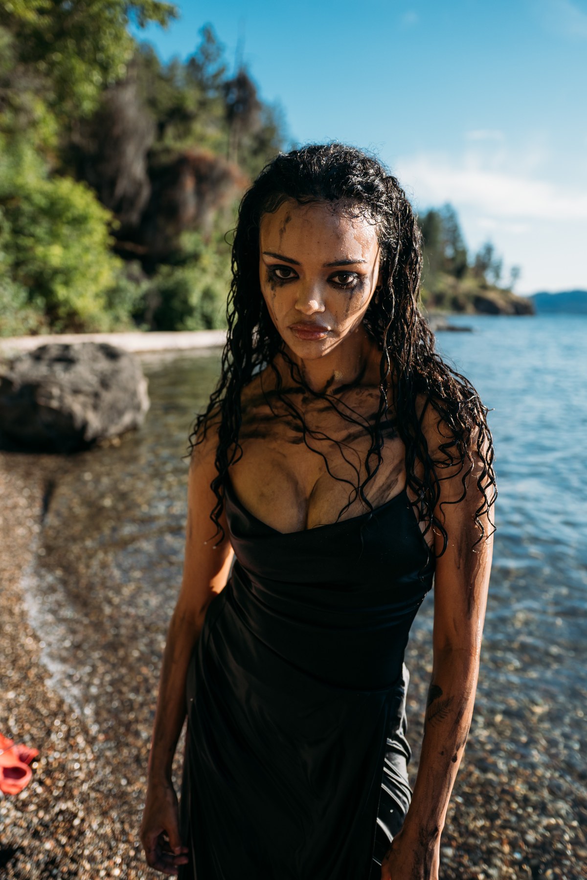 Alex by the Lake portraits story frame 9: Okanagan Lake portraits in Kelowna with black summer styling, rock, water, wind, direct expression and a cinematic beauty-portrait edge.