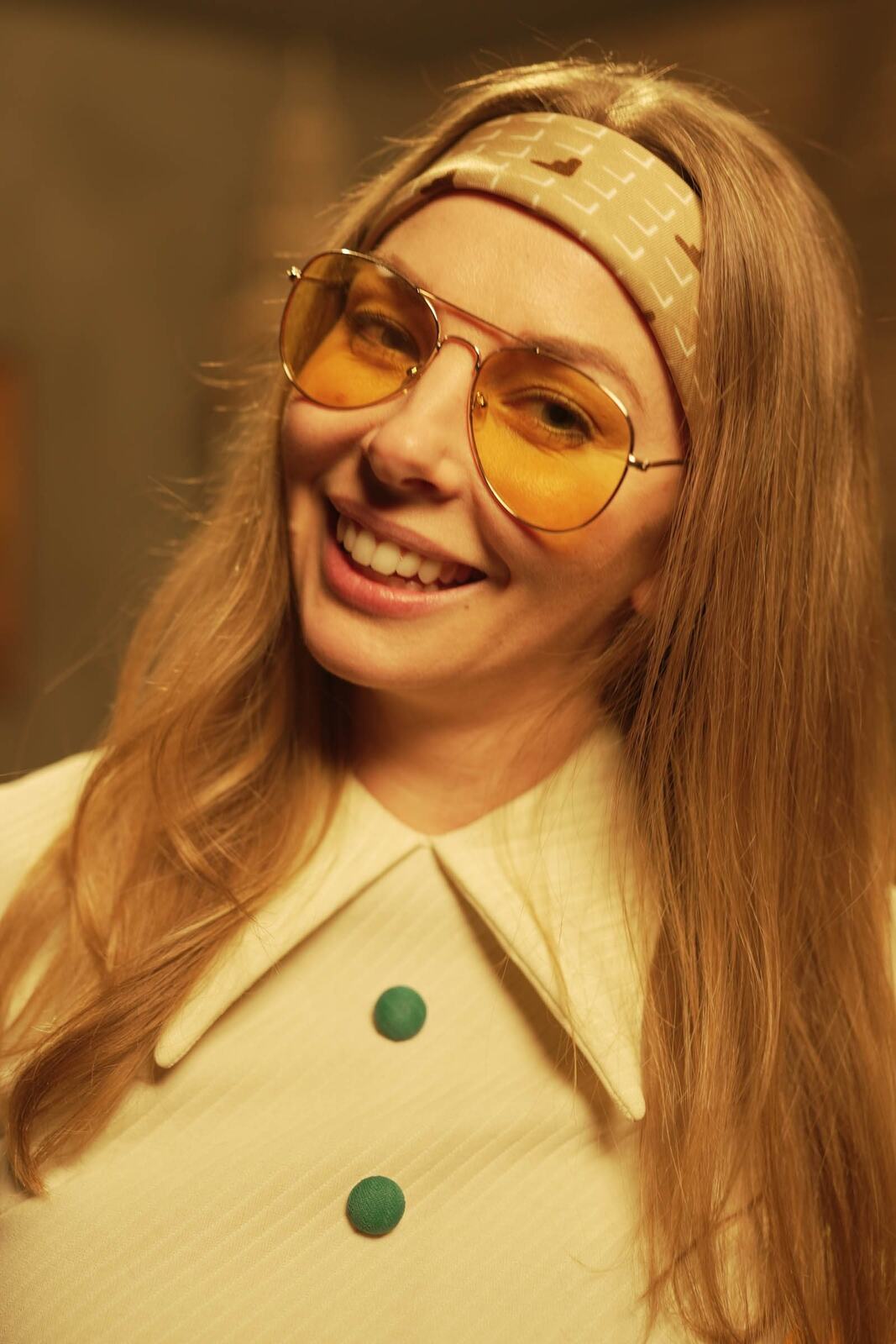 Angela in the 70s Lounge portraits story frame 2: A warm 70s lounge portrait story with yellow glasses, retro styling, couch texture and a softer studio mood.