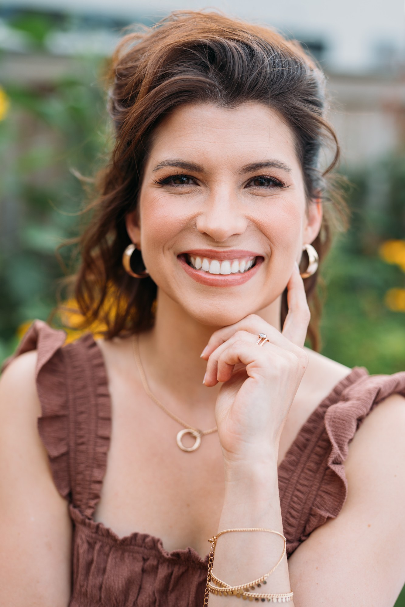 Marie smiling in a brown dress with styled hair and makeup in the garden.
