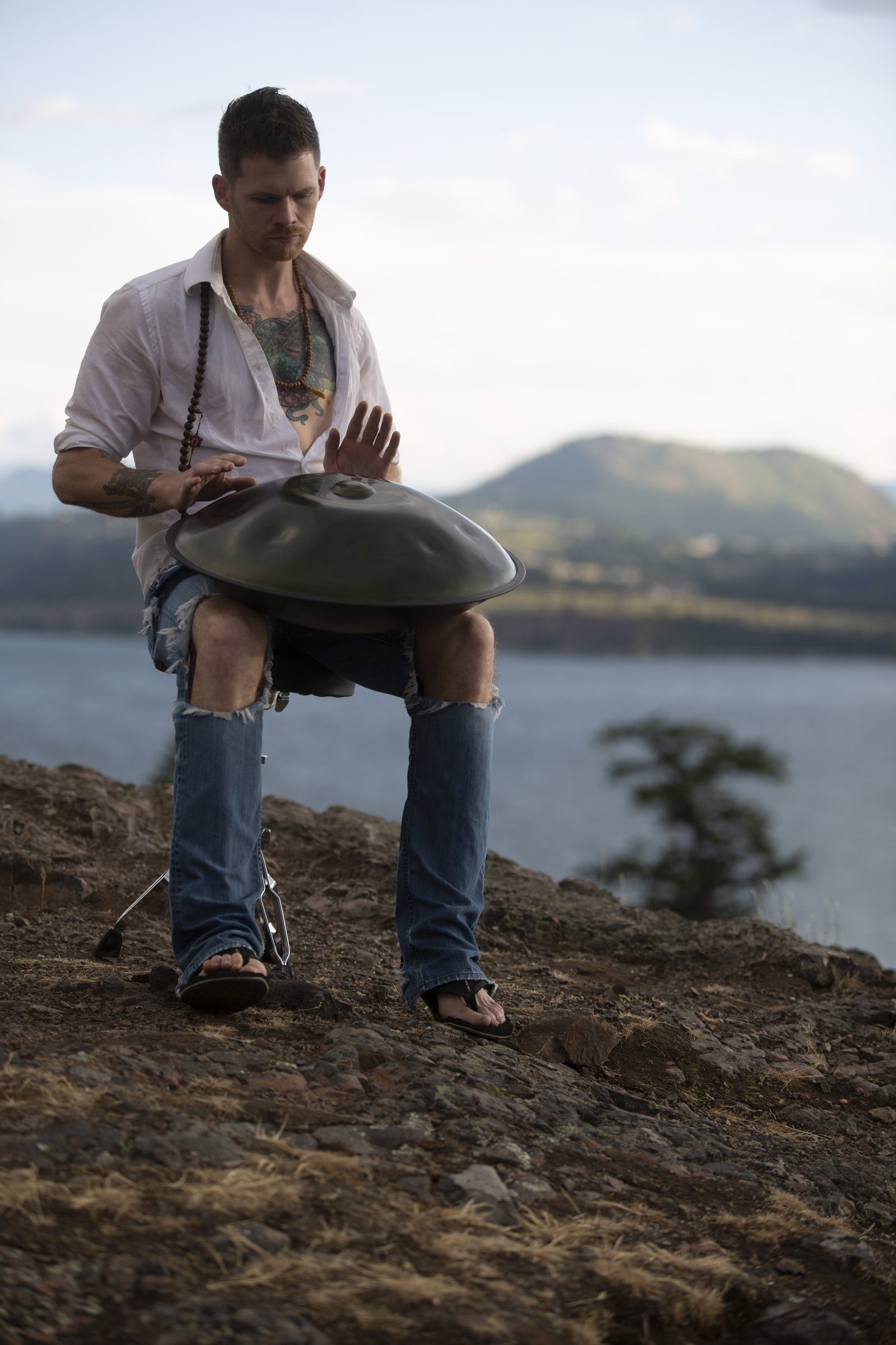 A vertical portrait of Jacob playing handpan at the lake overlook.