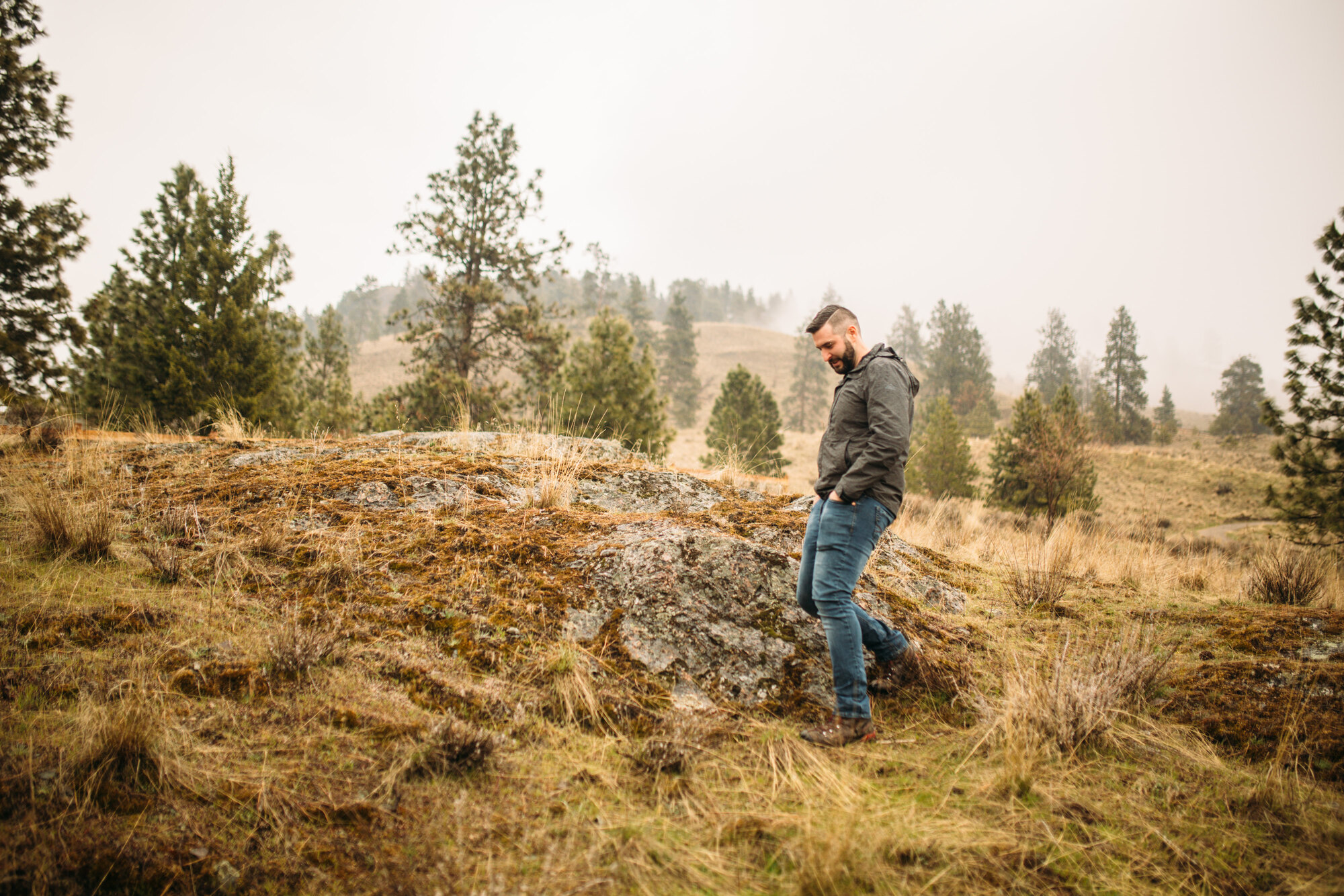 Very distant portrait of Jeremy standing alone in the Knox Mountain grassland.