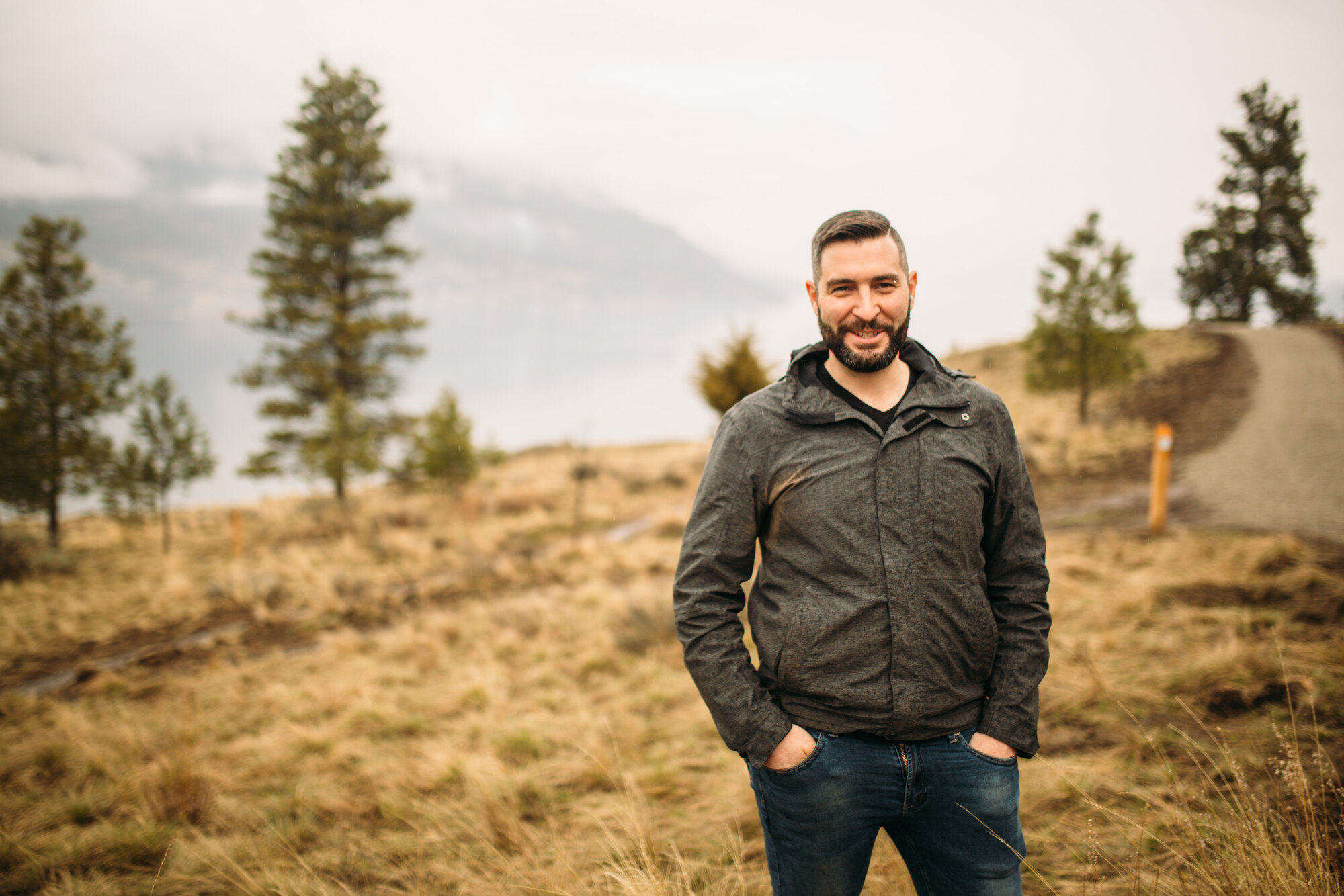 Jeremy standing in an open landscape portrait with lake and trees behind him.