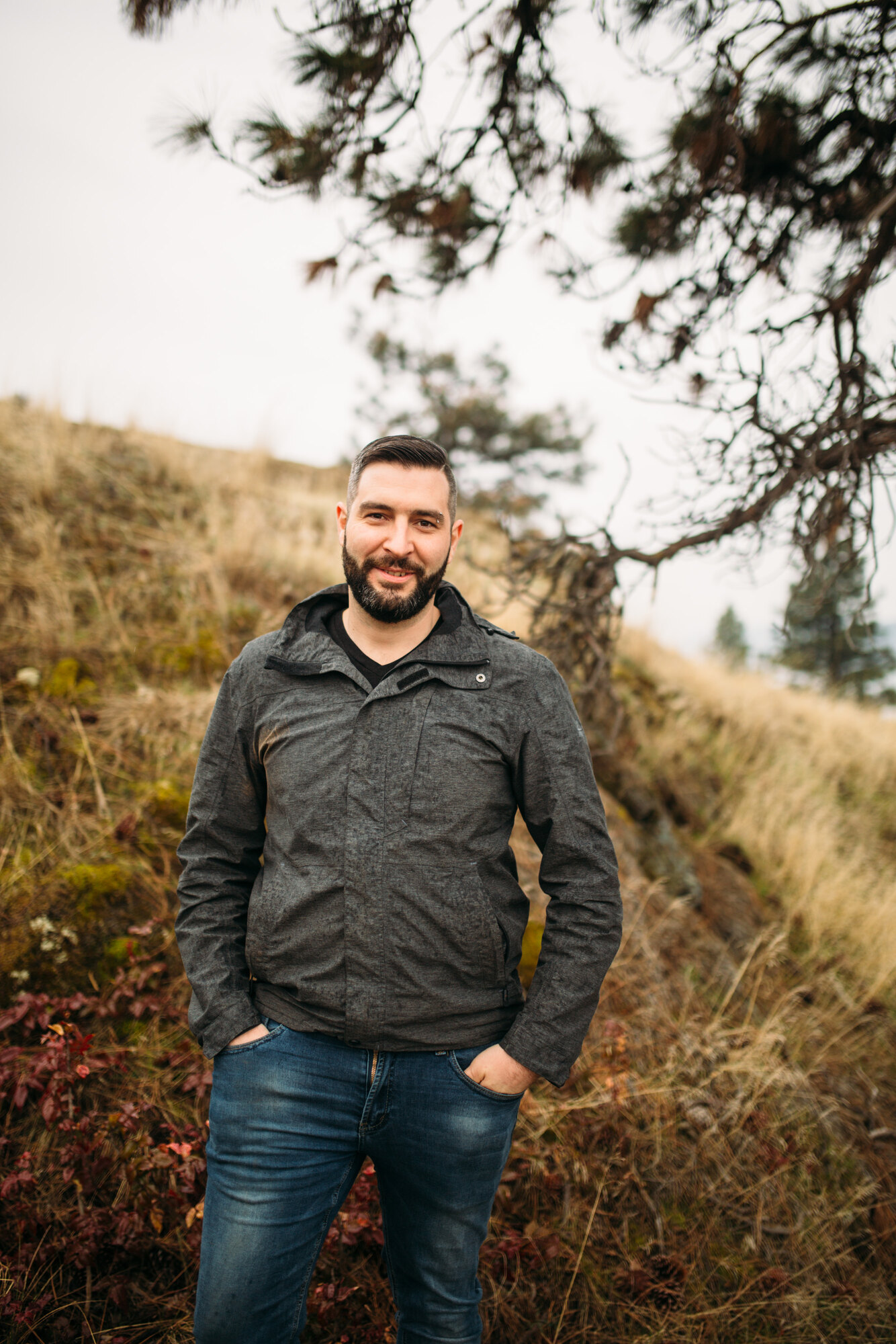 Vertical full-body portrait of Jeremy under tree branches on Knox Mountain.