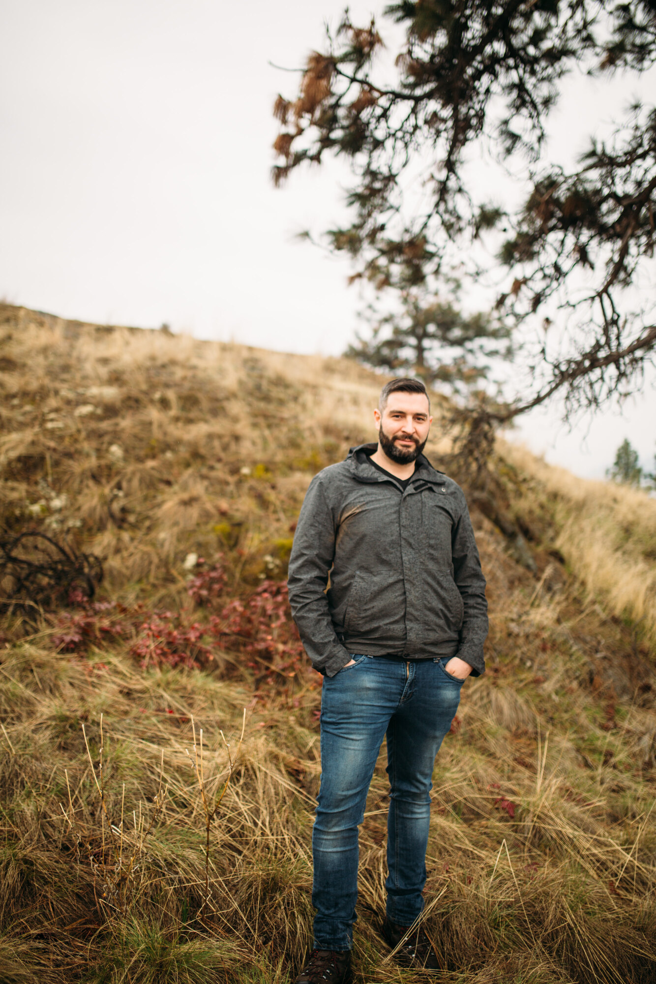 Vertical outdoor portrait of Jeremy standing in red brush and dry grass.