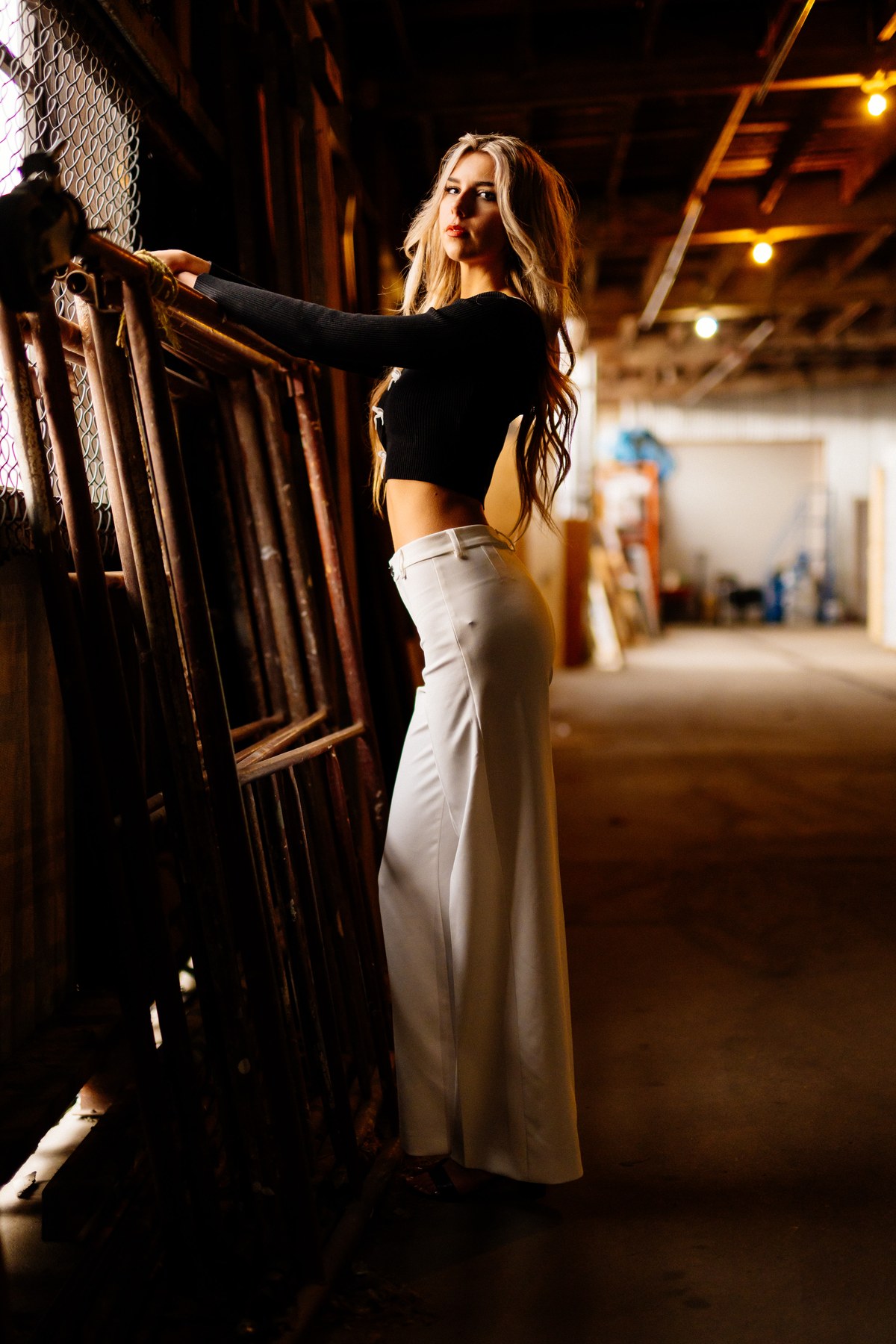 Kaylee in Clouds portraits story frame 3: Kelowna studio portraits with cloud styling, warm industrial light, black lace-up wardrobe, white pants and soft editorial glamour.