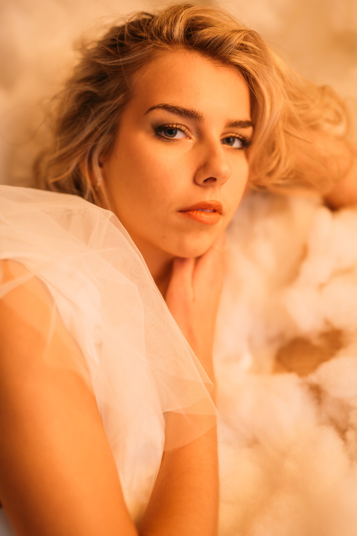 Kaylee in Clouds portraits story frame 7: Kelowna studio portraits with cloud styling, warm industrial light, black lace-up wardrobe, white pants and soft editorial glamour.