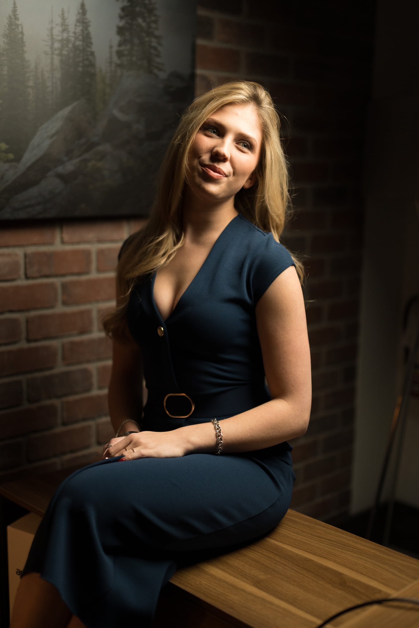 Kennedy seated beside the brick wall in a navy dress