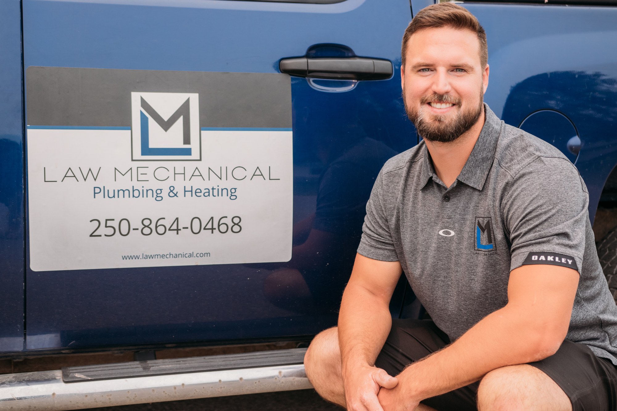 Law Mechanical: Relaxed crouched portrait beside the branded blue truck.