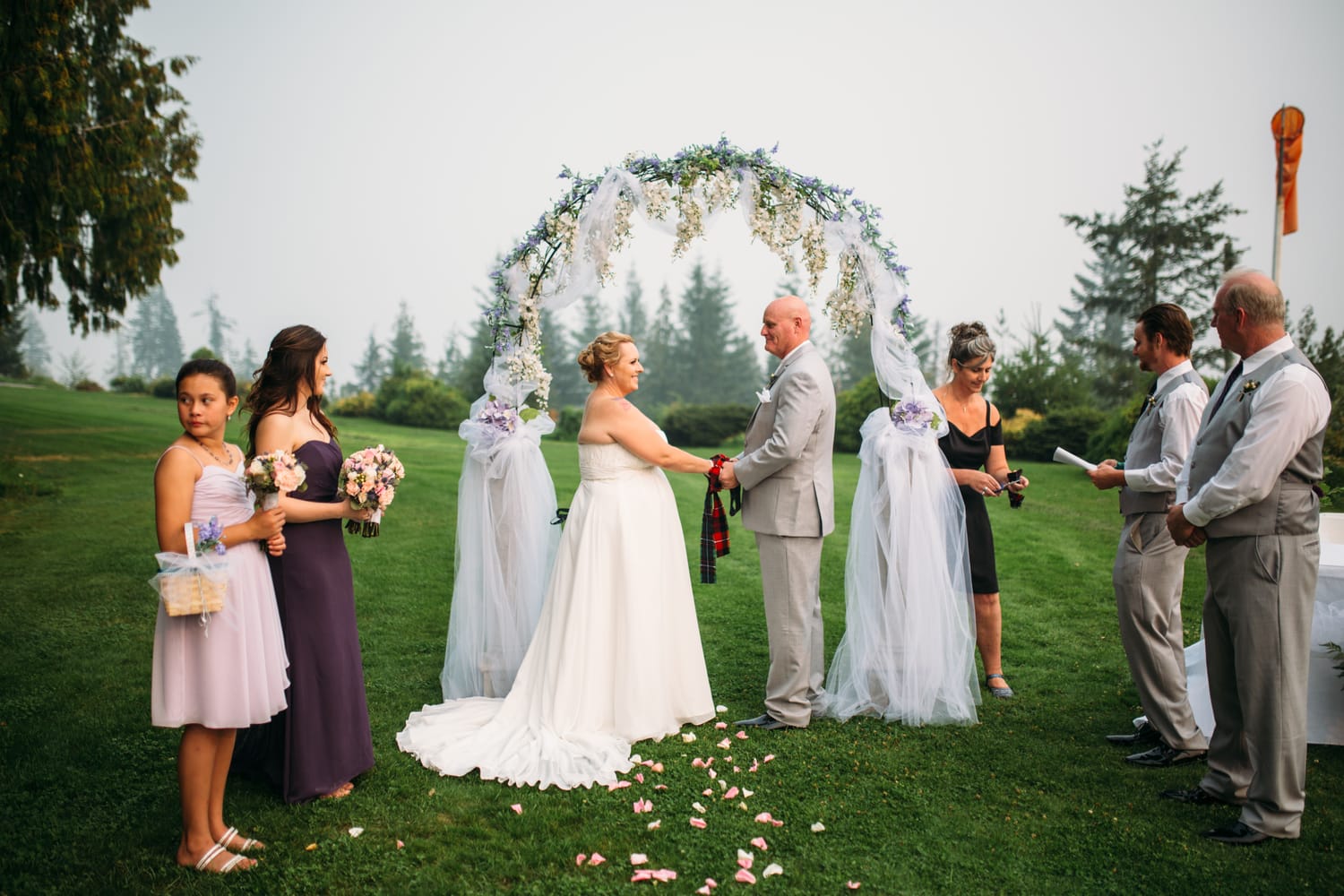 Marie and Mark weddings story frame 21: A Mabel Lake Airpark wedding in the North Okanagan, with grass-runway scenery, open-air photos and sweet family help around makeup, flowers and petals..