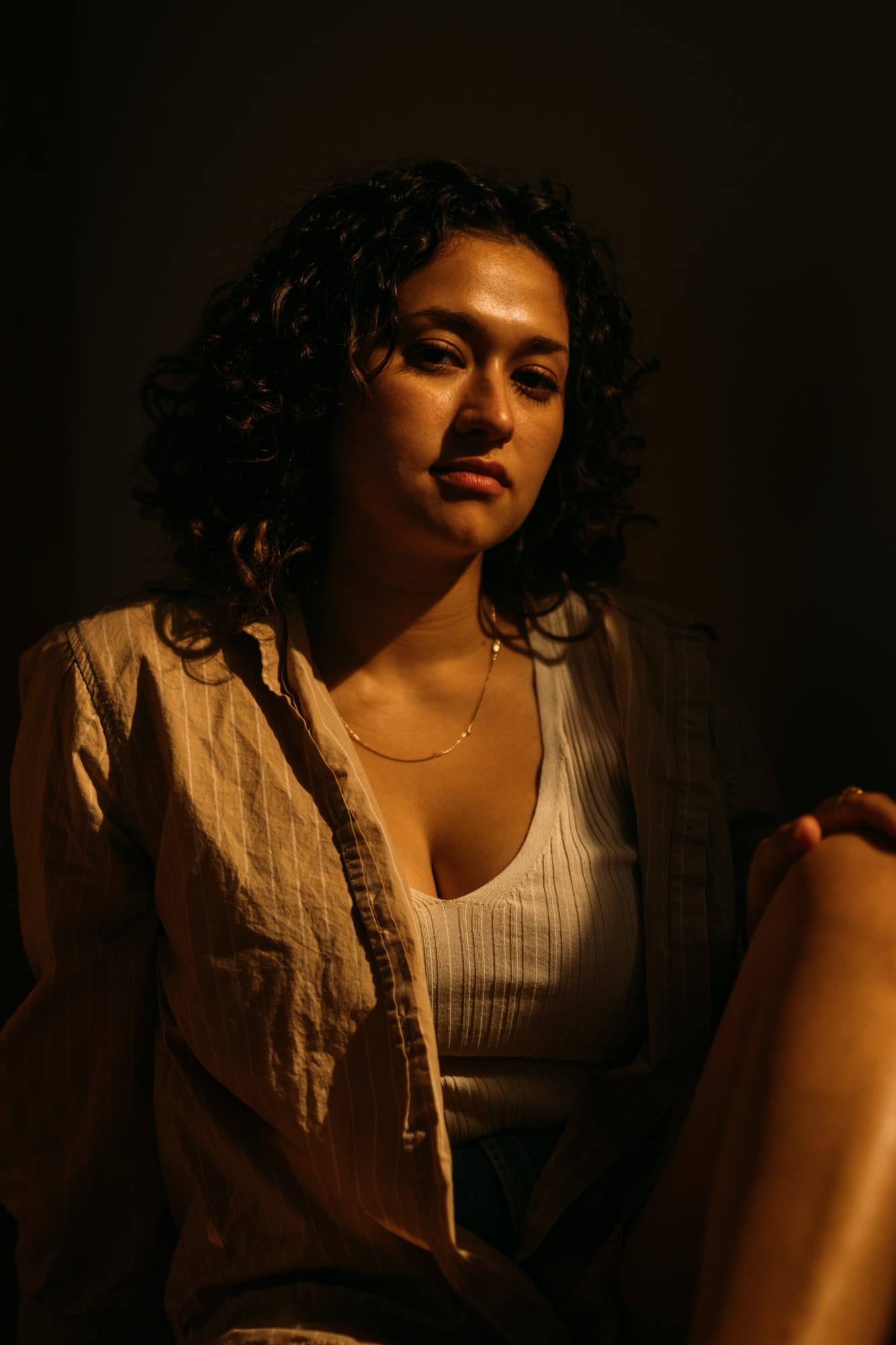 Marina in Warm Window Light portraits story frame 3: Marina in warm indoor light, with amber shadow, denim, black robe, green styling and an intimate editorial portrait mood.
