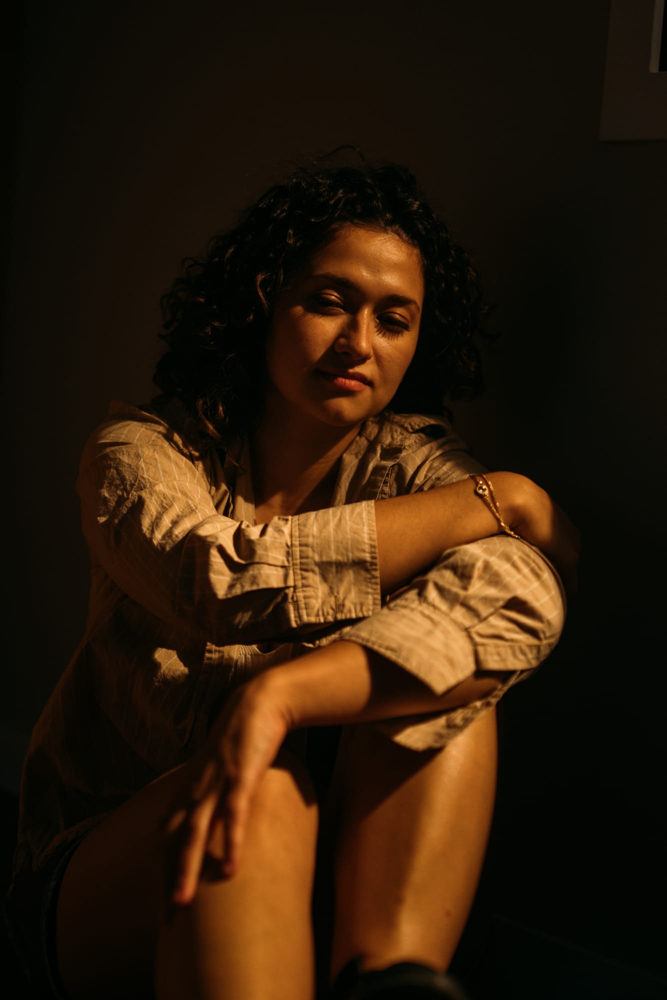 Marina in Warm Window Light portraits story frame 4: Marina in warm indoor light, with amber shadow, denim, black robe, green styling and an intimate editorial portrait mood.
