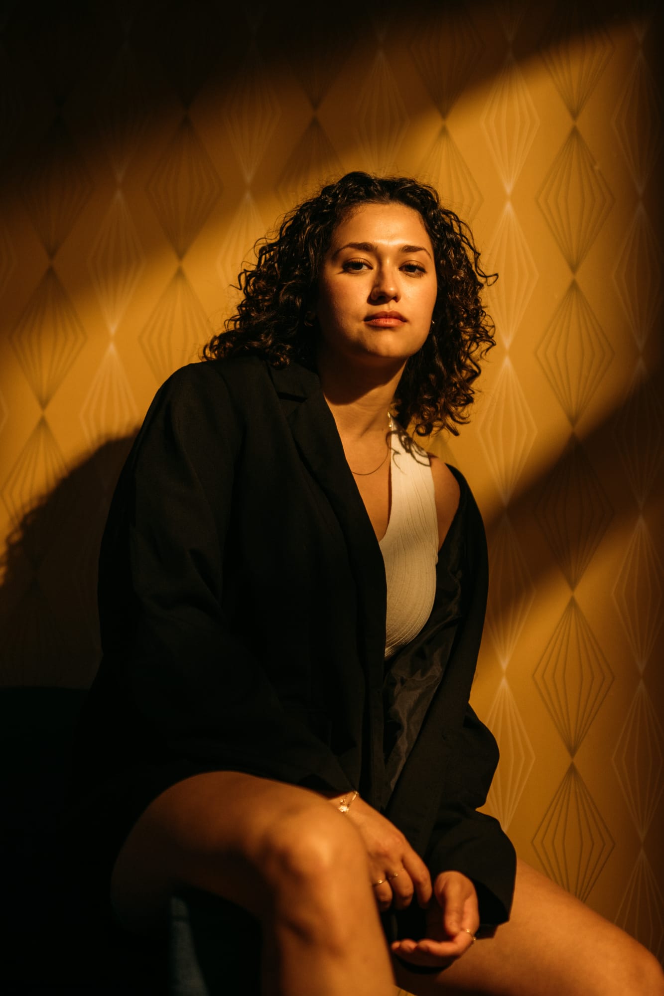 Marina in Warm Window Light portraits story frame 5: Marina in warm indoor light, with amber shadow, denim, black robe, green styling and an intimate editorial portrait mood.