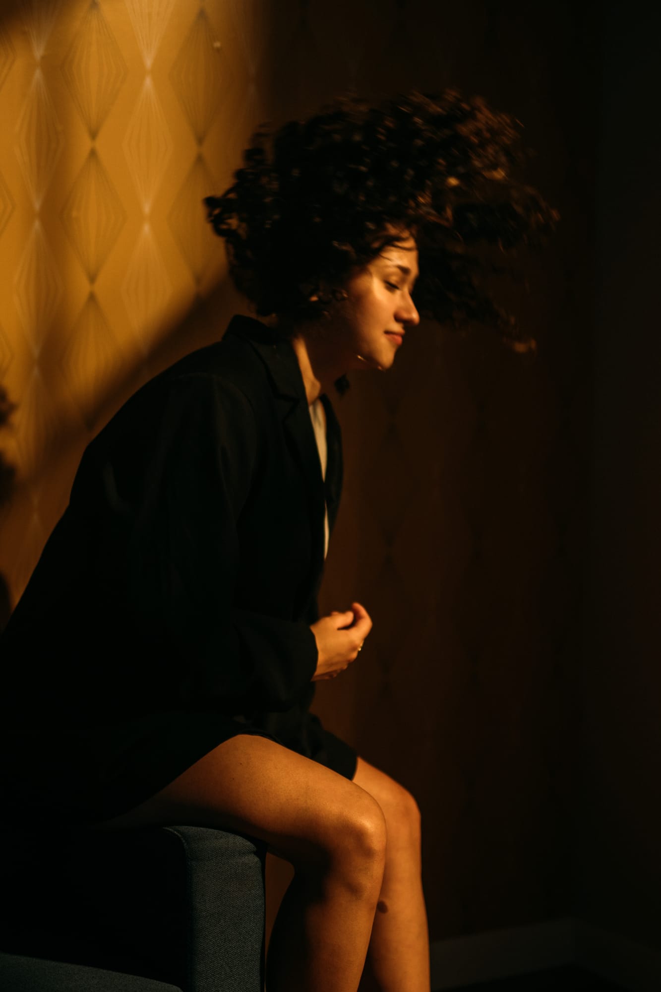 Marina in Warm Window Light portraits story frame 6: Marina in warm indoor light, with amber shadow, denim, black robe, green styling and an intimate editorial portrait mood.