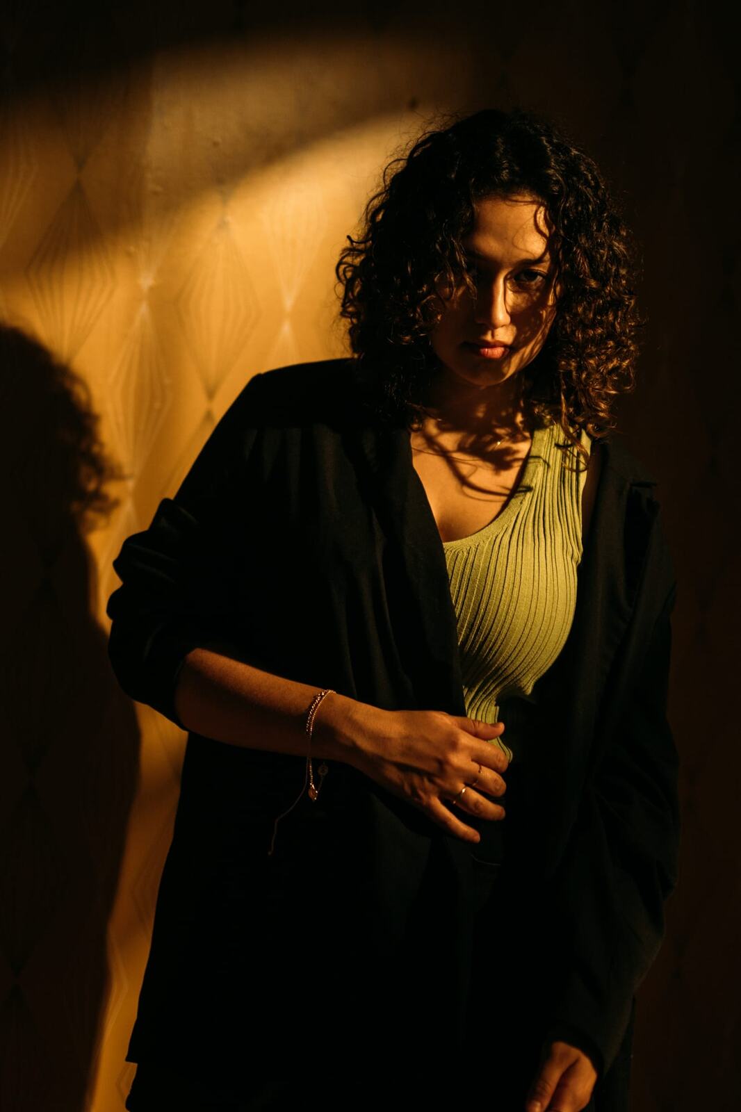 Marina in Warm Window Light portraits story frame 9: Marina in warm indoor light, with amber shadow, denim, black robe, green styling and an intimate editorial portrait mood.
