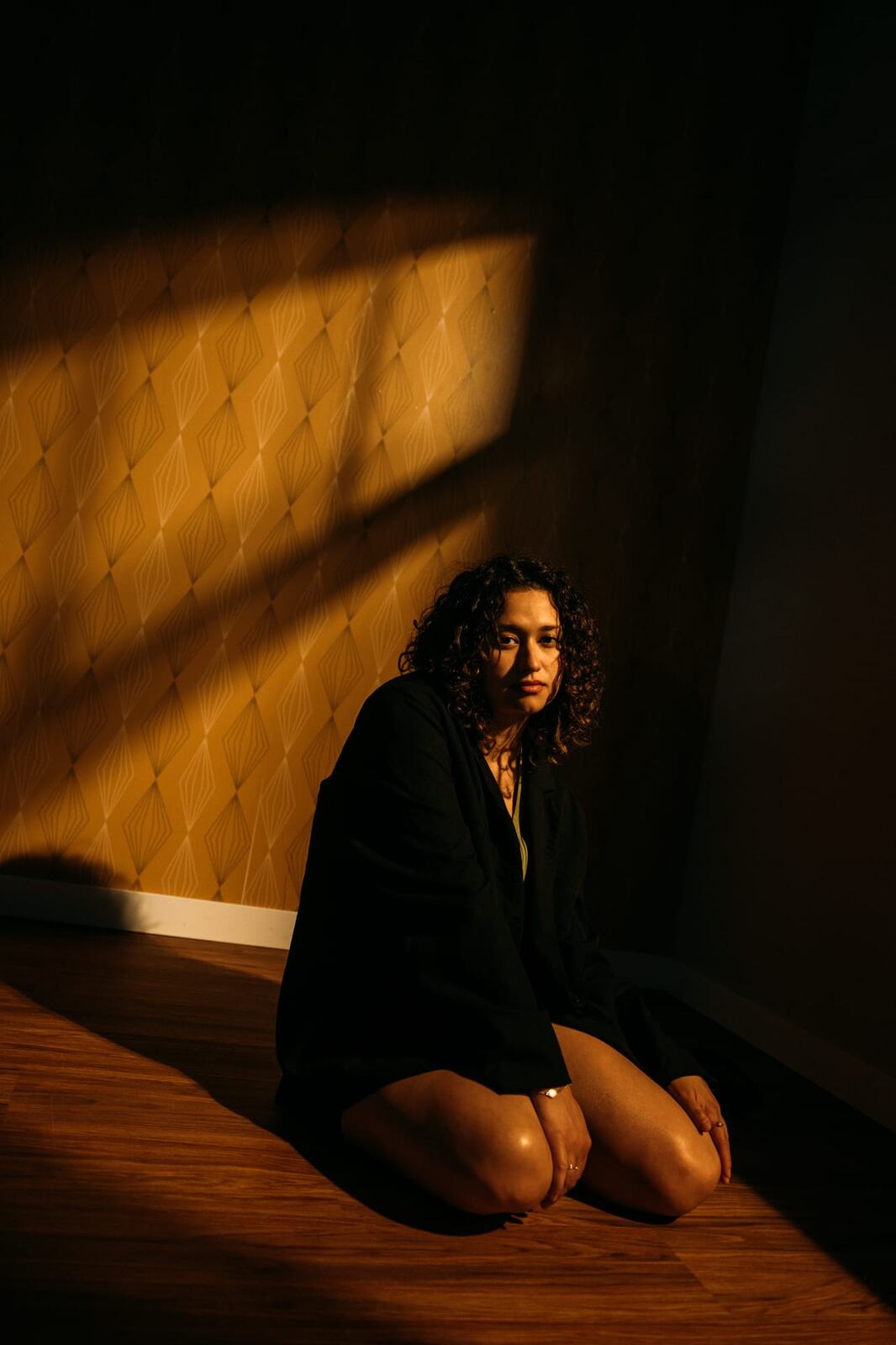 Marina in Warm Window Light portraits story frame 10: Marina in warm indoor light, with amber shadow, denim, black robe, green styling and an intimate editorial portrait mood.