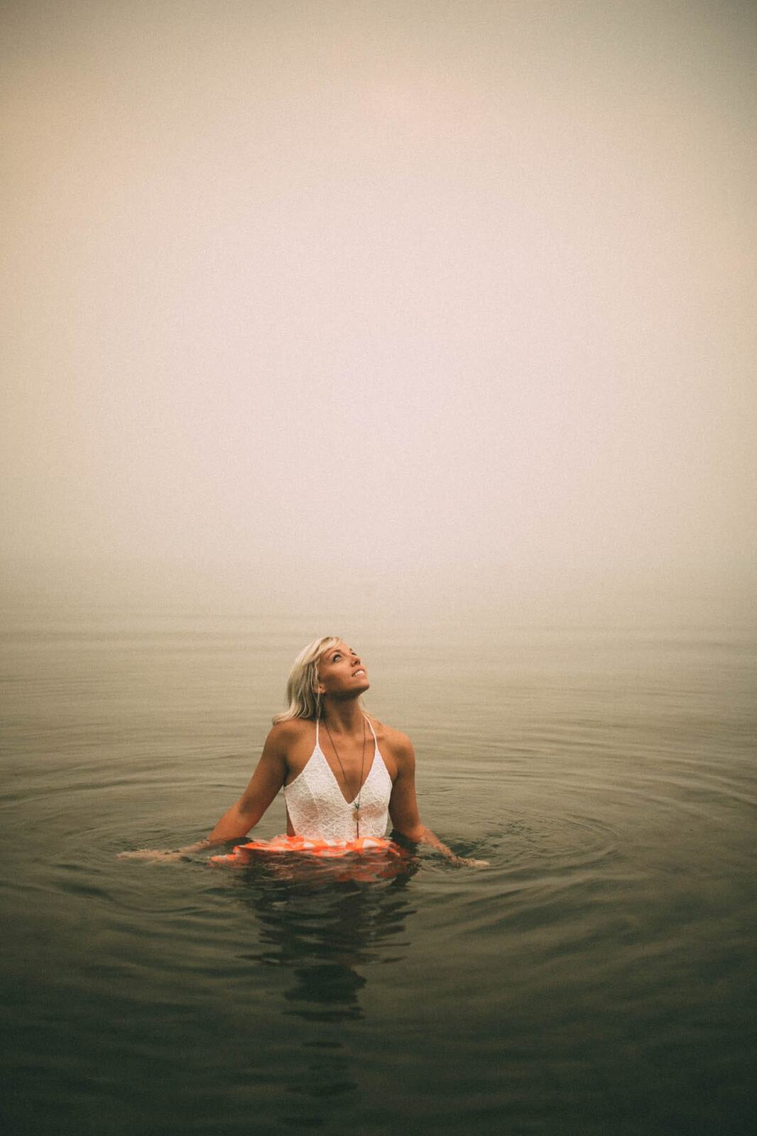 Megan Shallow portraits story frame 8: A fog-soft Kelowna lake portrait session for Megan Shallow, with water, orange dress movement, close body-language frames and quiet birds cutting through the mist.