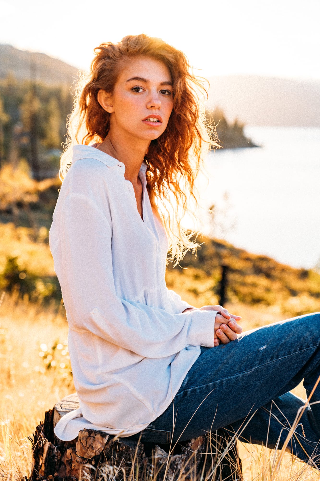 Mickie portraits story frame 2: A Kelowna portrait session for Mickie moving from golden grass and warm hillside light into lake-edge rocks, wind, white shirt styling and close editorial portraits.