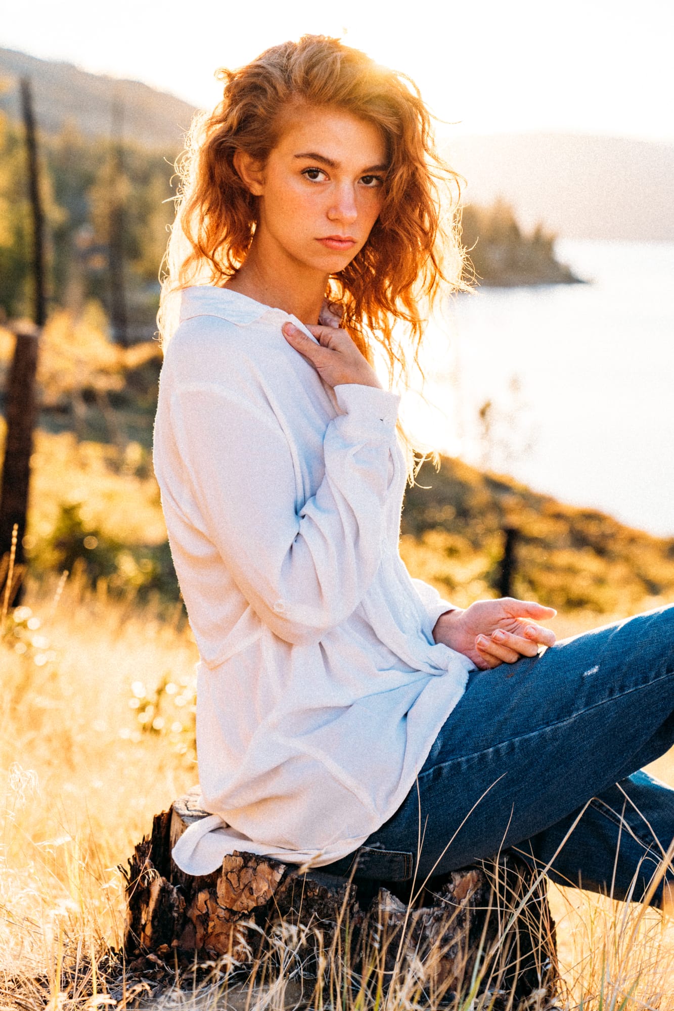 Mickie portraits story frame 3: A Kelowna portrait session for Mickie moving from golden grass and warm hillside light into lake-edge rocks, wind, white shirt styling and close editorial portraits.