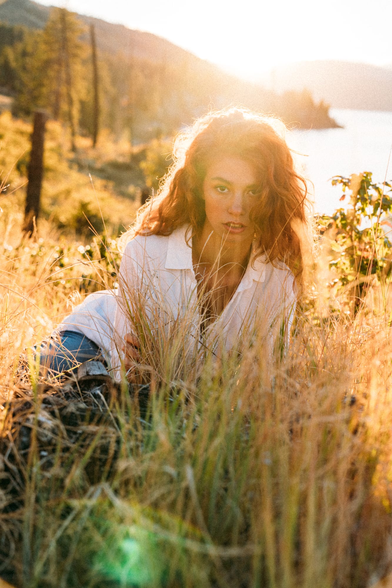 Mickie portraits story frame 4: A Kelowna portrait session for Mickie moving from golden grass and warm hillside light into lake-edge rocks, wind, white shirt styling and close editorial portraits.