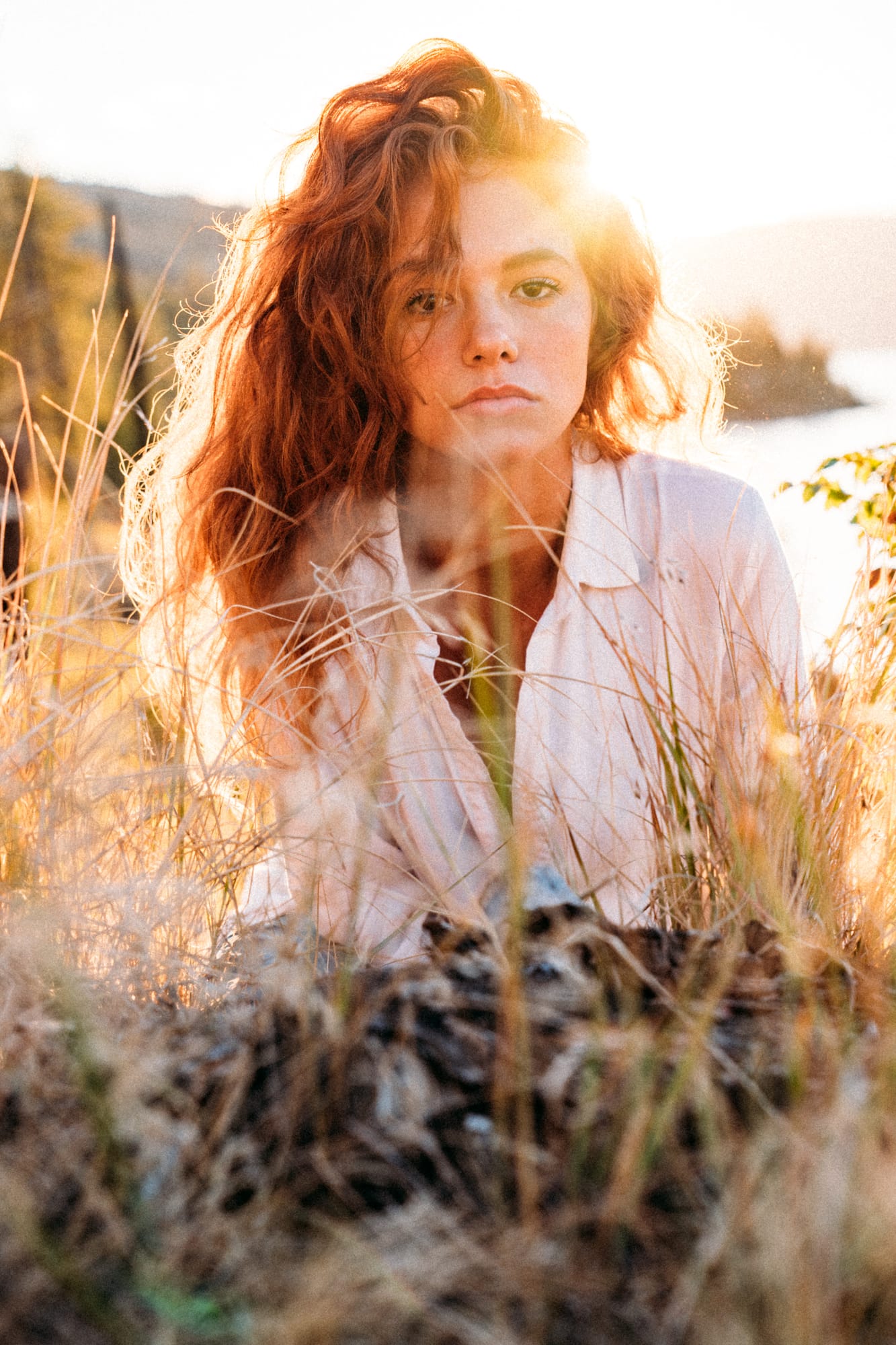 Mickie portraits story frame 5: A Kelowna portrait session for Mickie moving from golden grass and warm hillside light into lake-edge rocks, wind, white shirt styling and close editorial portraits.