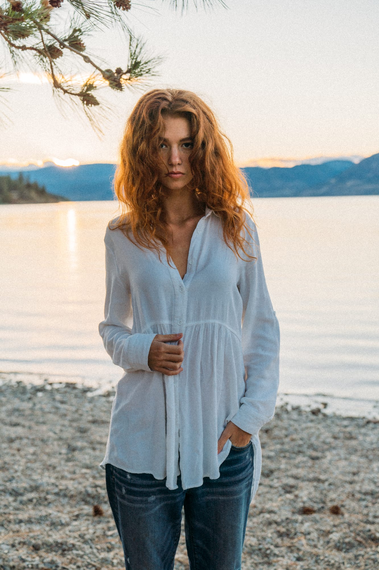 Mickie portraits story frame 12: A Kelowna portrait session for Mickie moving from golden grass and warm hillside light into lake-edge rocks, wind, white shirt styling and close editorial portraits.
