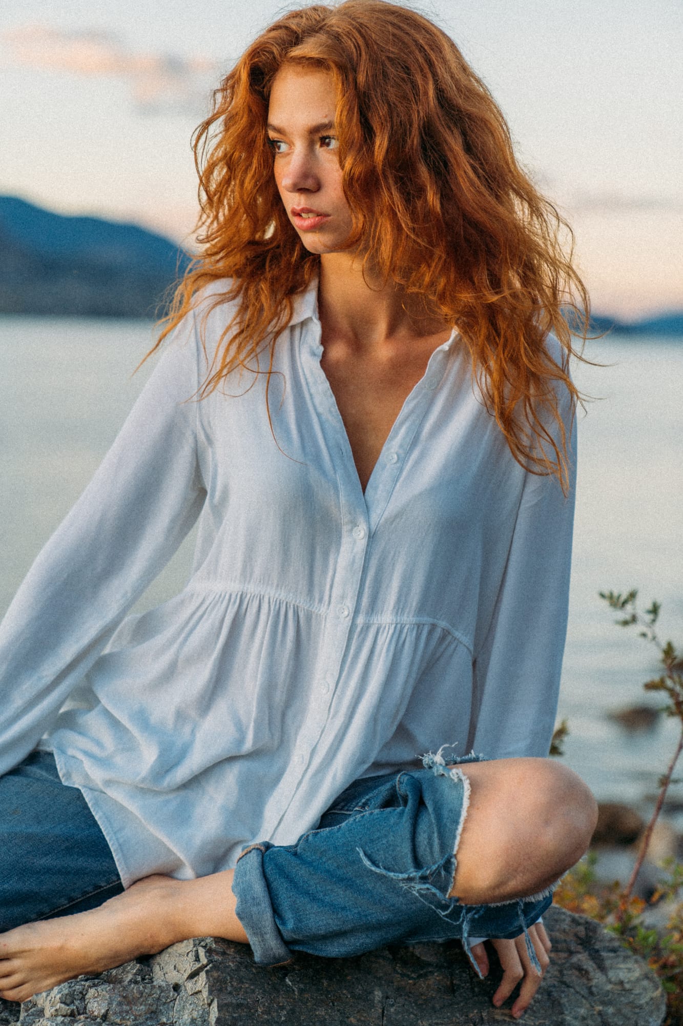 Mickie portraits story frame 13: A Kelowna portrait session for Mickie moving from golden grass and warm hillside light into lake-edge rocks, wind, white shirt styling and close editorial portraits.