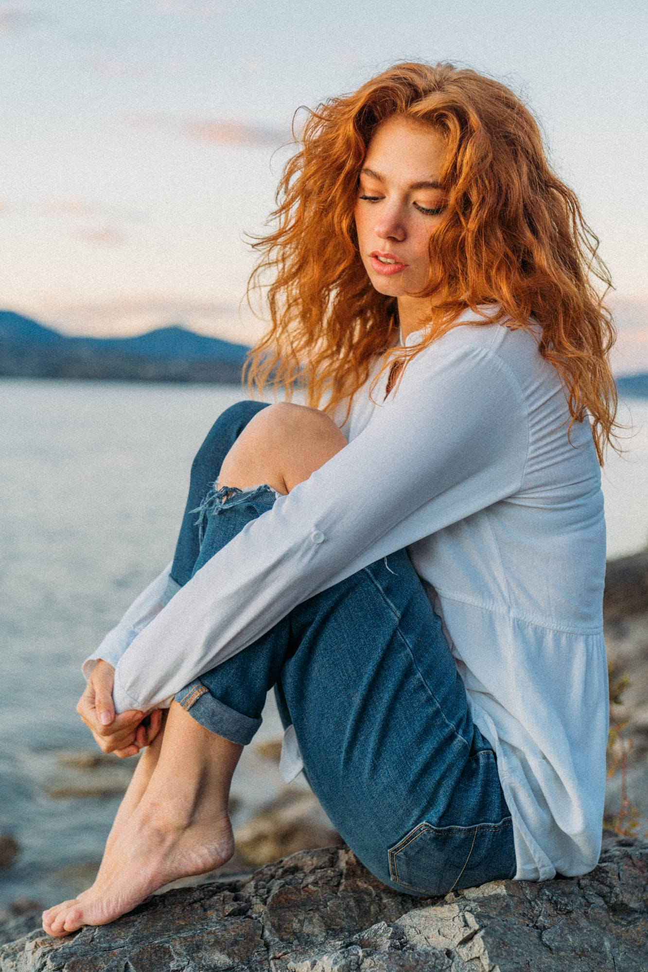 Mickie portraits story frame 19: A Kelowna portrait session for Mickie moving from golden grass and warm hillside light into lake-edge rocks, wind, white shirt styling and close editorial portraits.