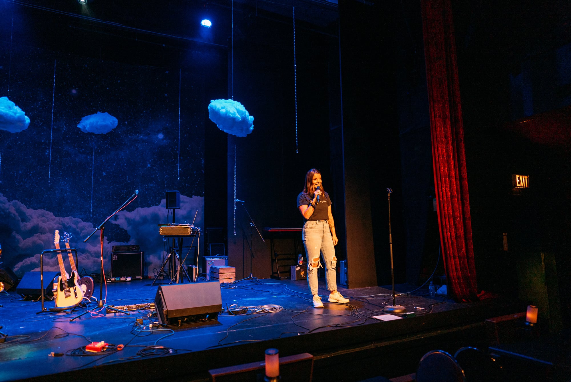 Wide blue-lit stage with a solo vocalist and instruments set at Kelowna Actors Studio.