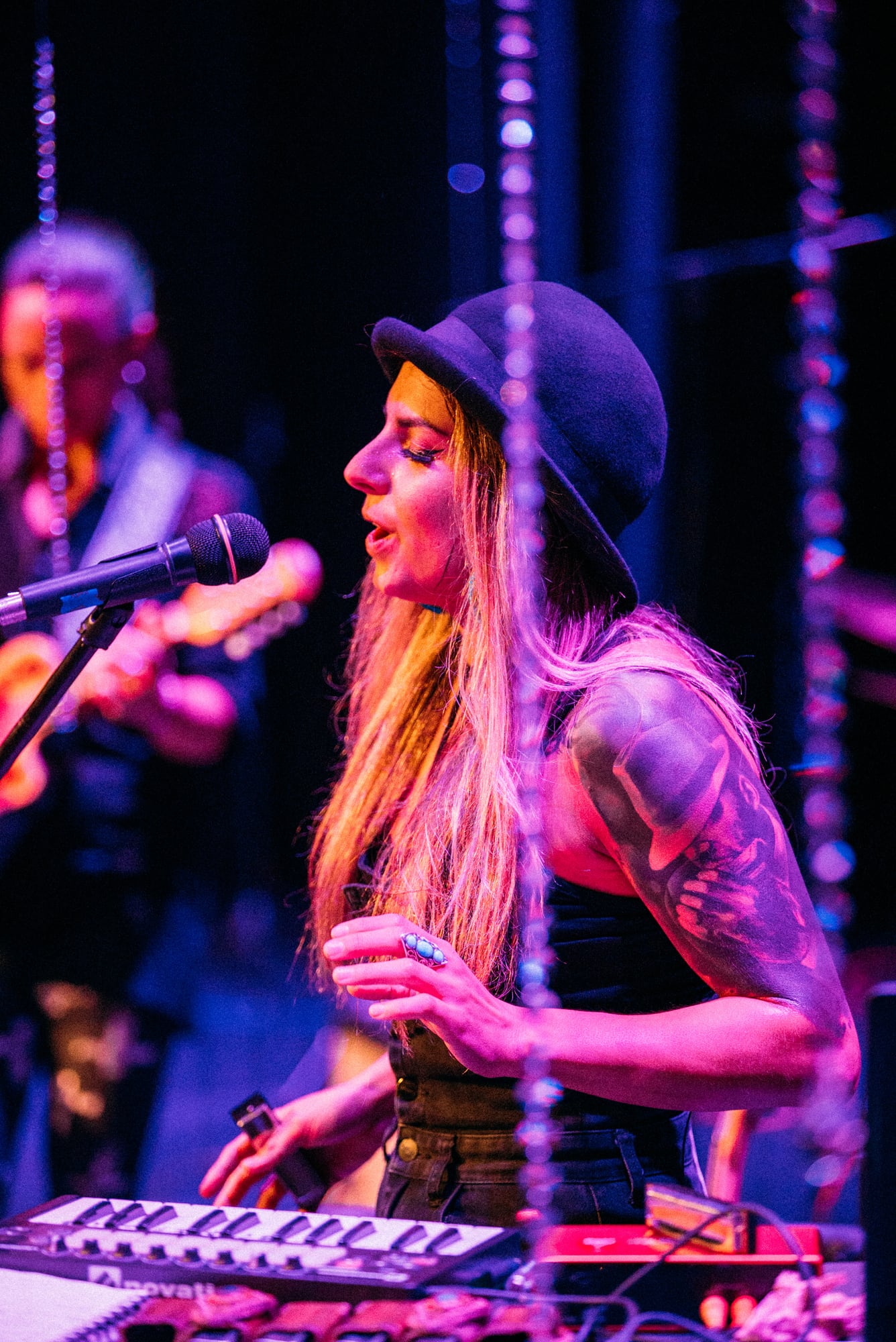 Performer at keyboard and microphone with another musician behind her.