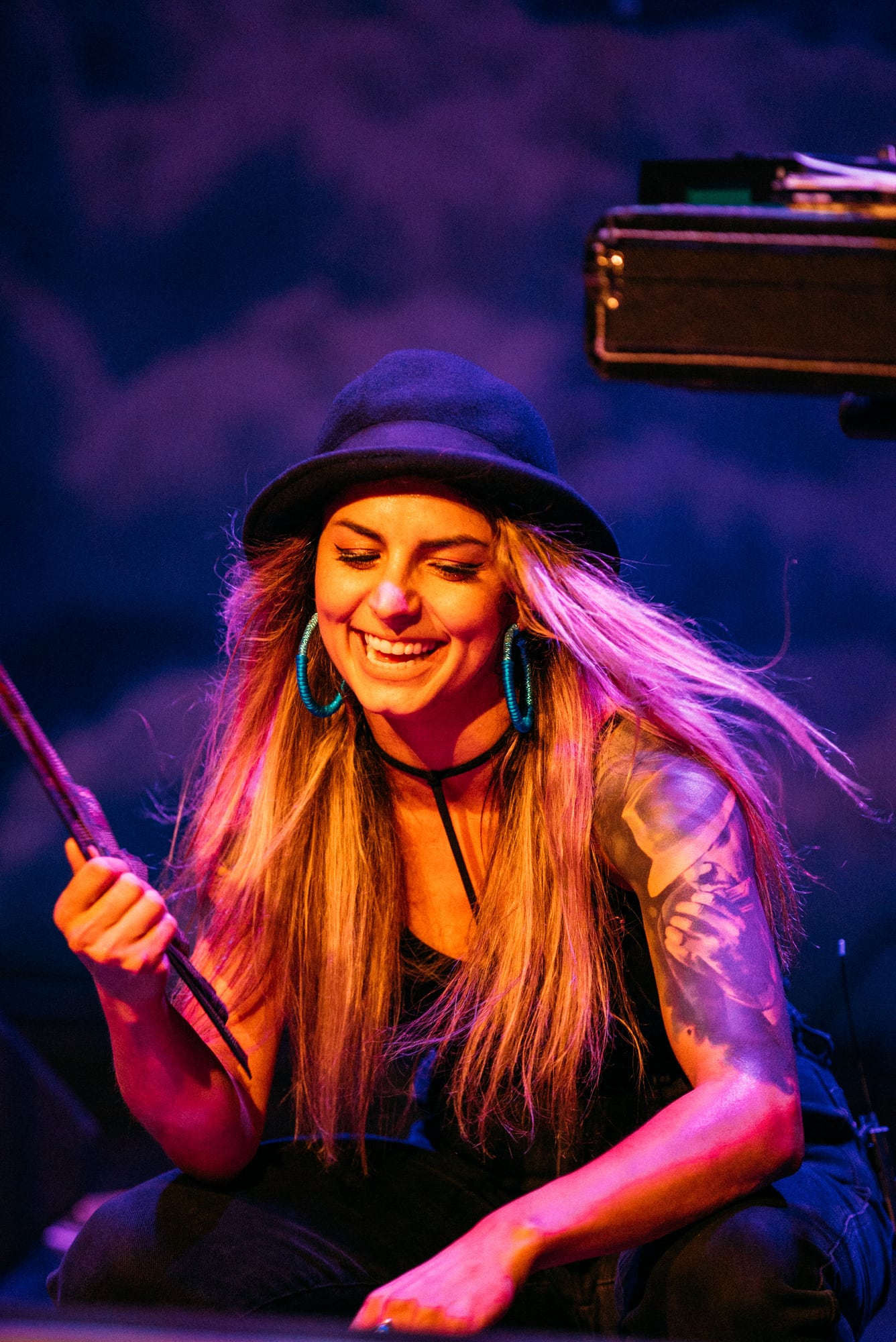 Smiling seated performer holding sticks beneath purple stage light.