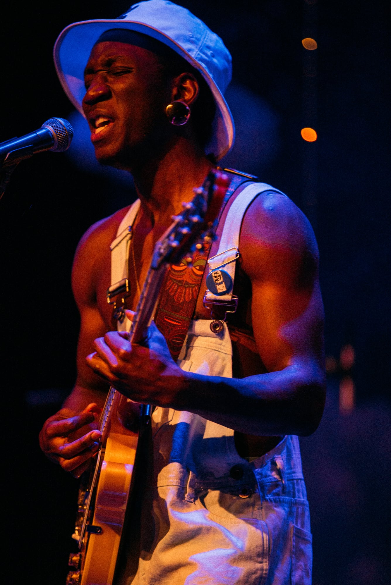 Guitarist singing in a white outfit under warm blue stage light.