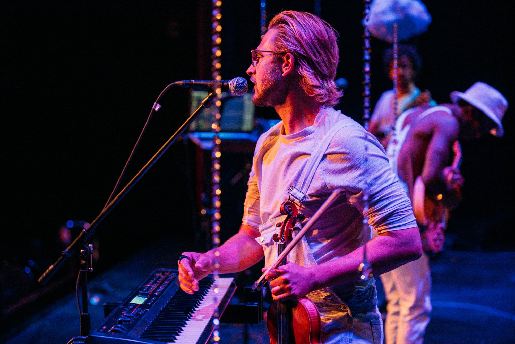 Guitarist at microphone in profile with cloud stage props behind.