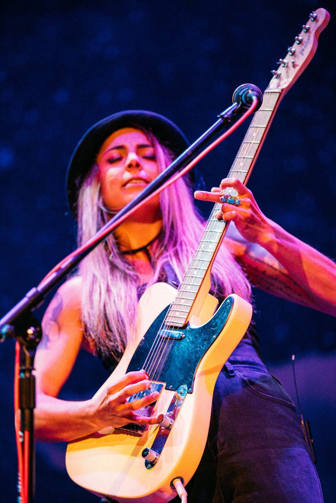 Guitarist at microphone in profile with cloud stage props behind.