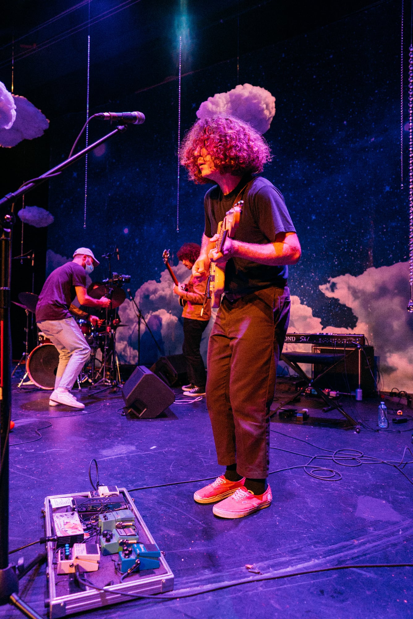 Guitarist stepping forward onstage with a pedal board in the foreground.