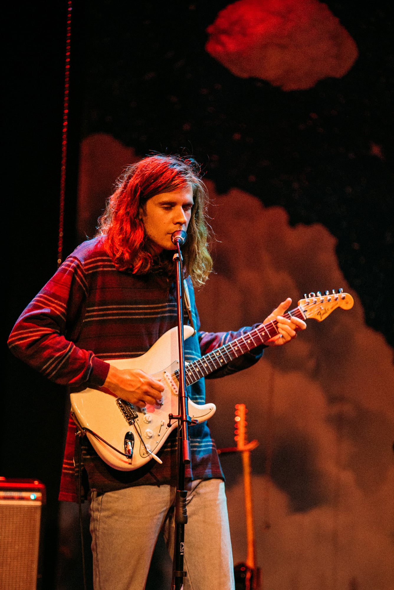 Guitarist in a striped shirt performing against warm smoke and shadow.