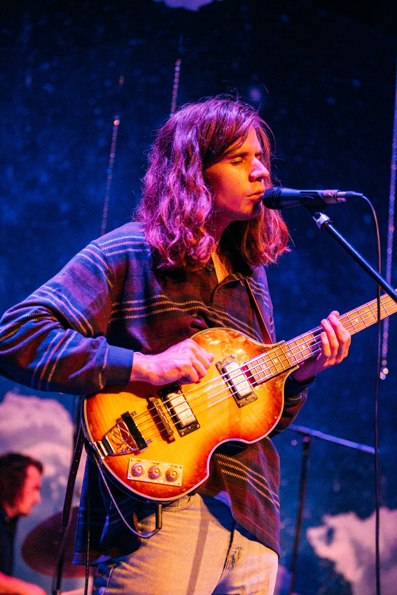 Bassist singing at microphone with drummer behind.