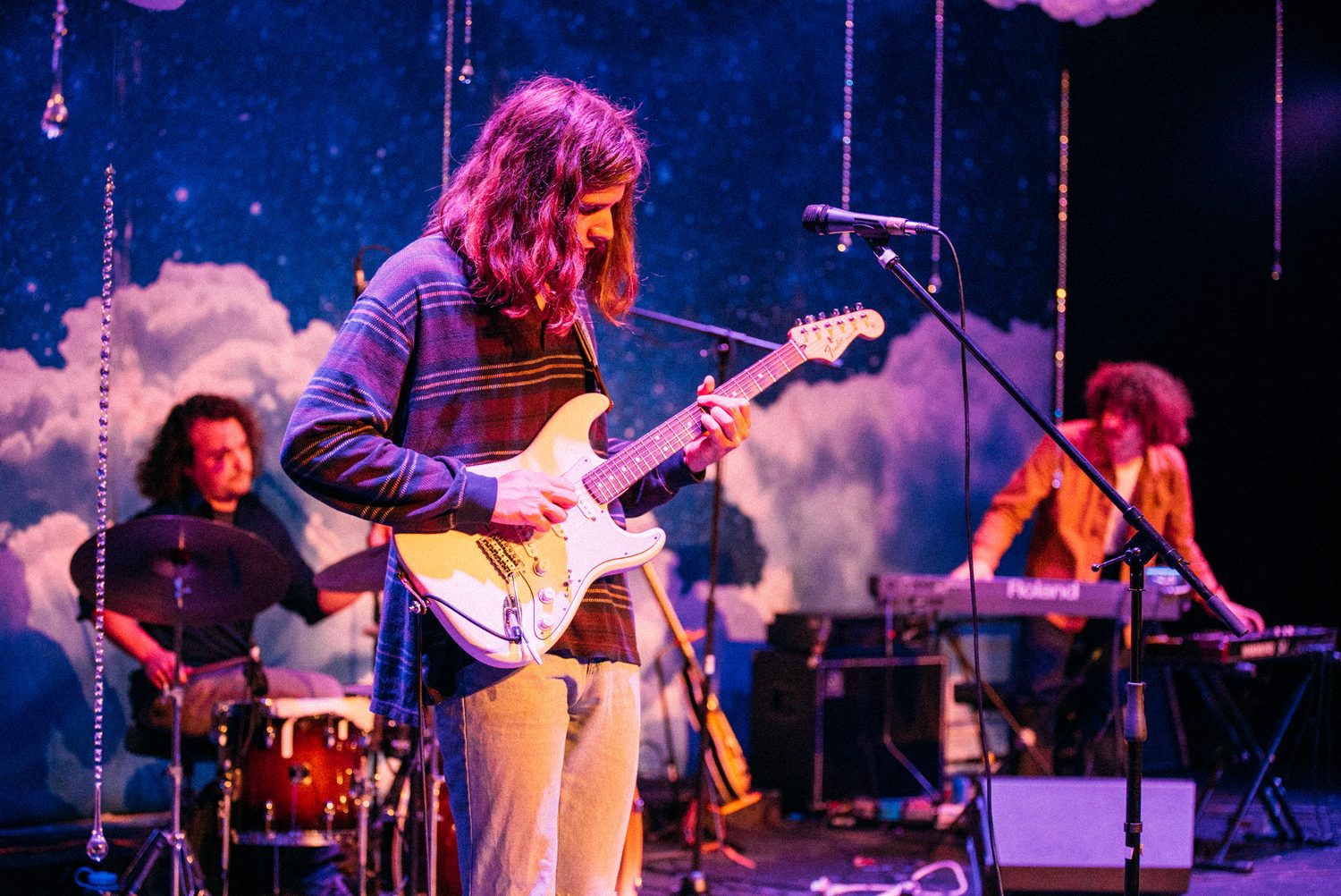 Wide blue-lit stage with a solo vocalist and instruments set at Kelowna Actors Studio.