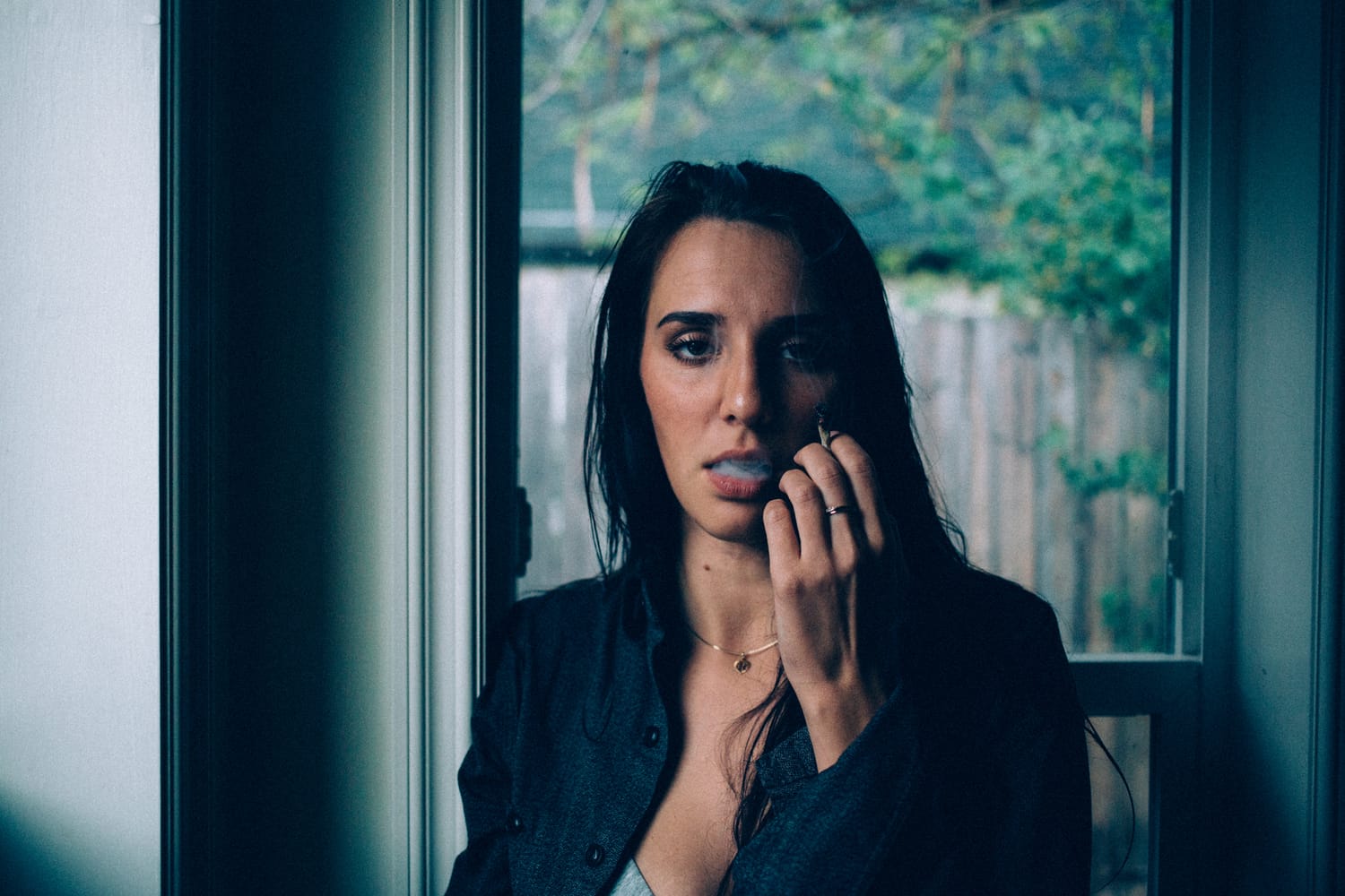 Rebecca in Smoke portraits story frame 24: A dark Kelowna portrait story for Rebecca with window light, smoke, denim, close expression and a low-key editorial mood.