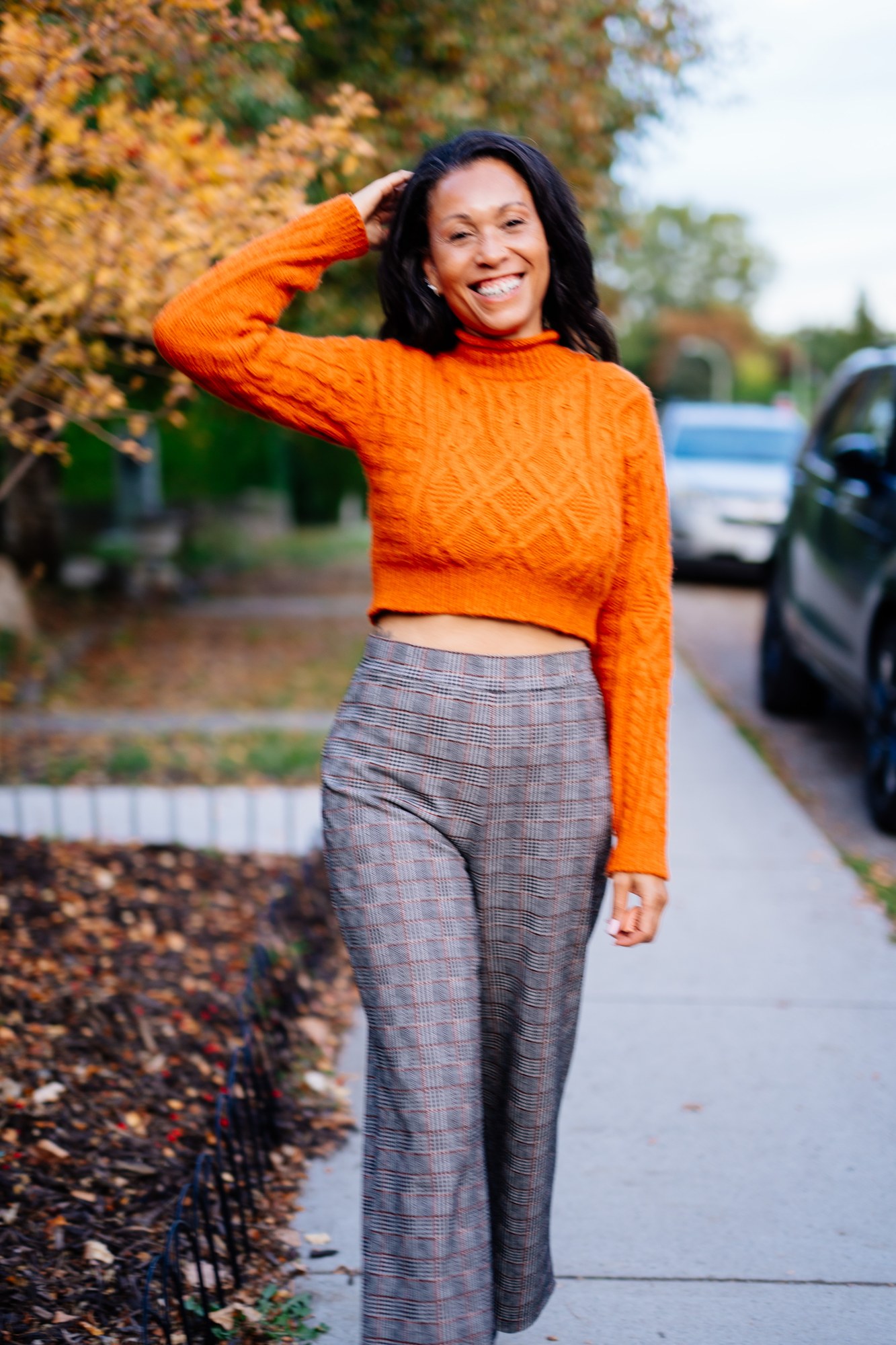 Rebekah in Autumn: Sidewalk portrait with one hand in hair and a warm smile.