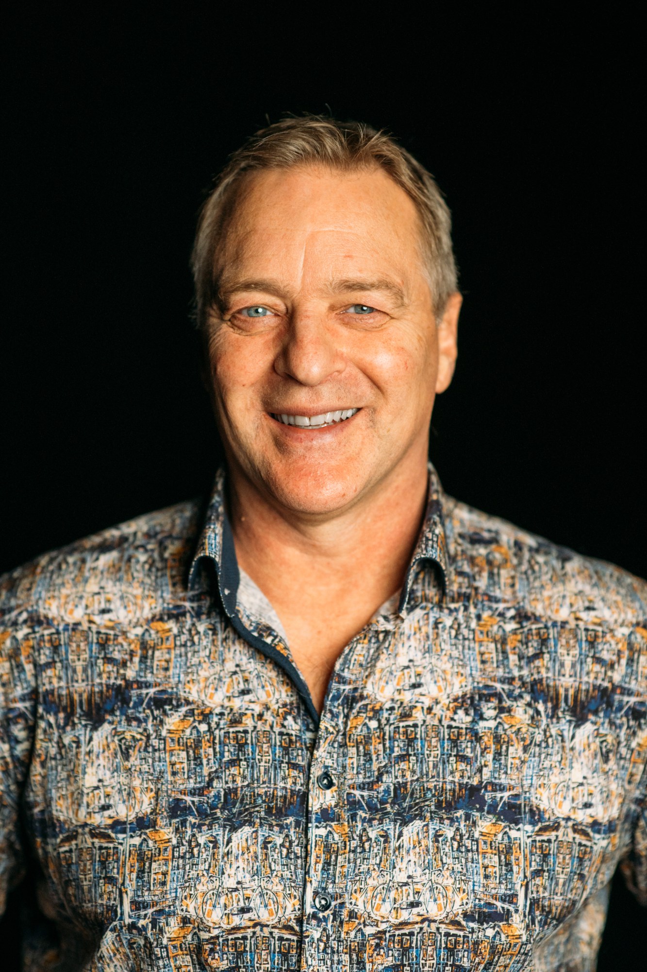 Roark Critchlow laughing in a patterned shirt against black