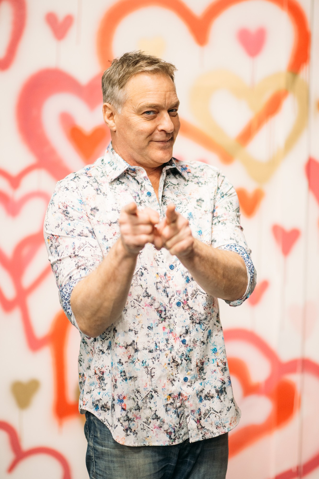 Roark making a playful hand gesture against a wall of hearts