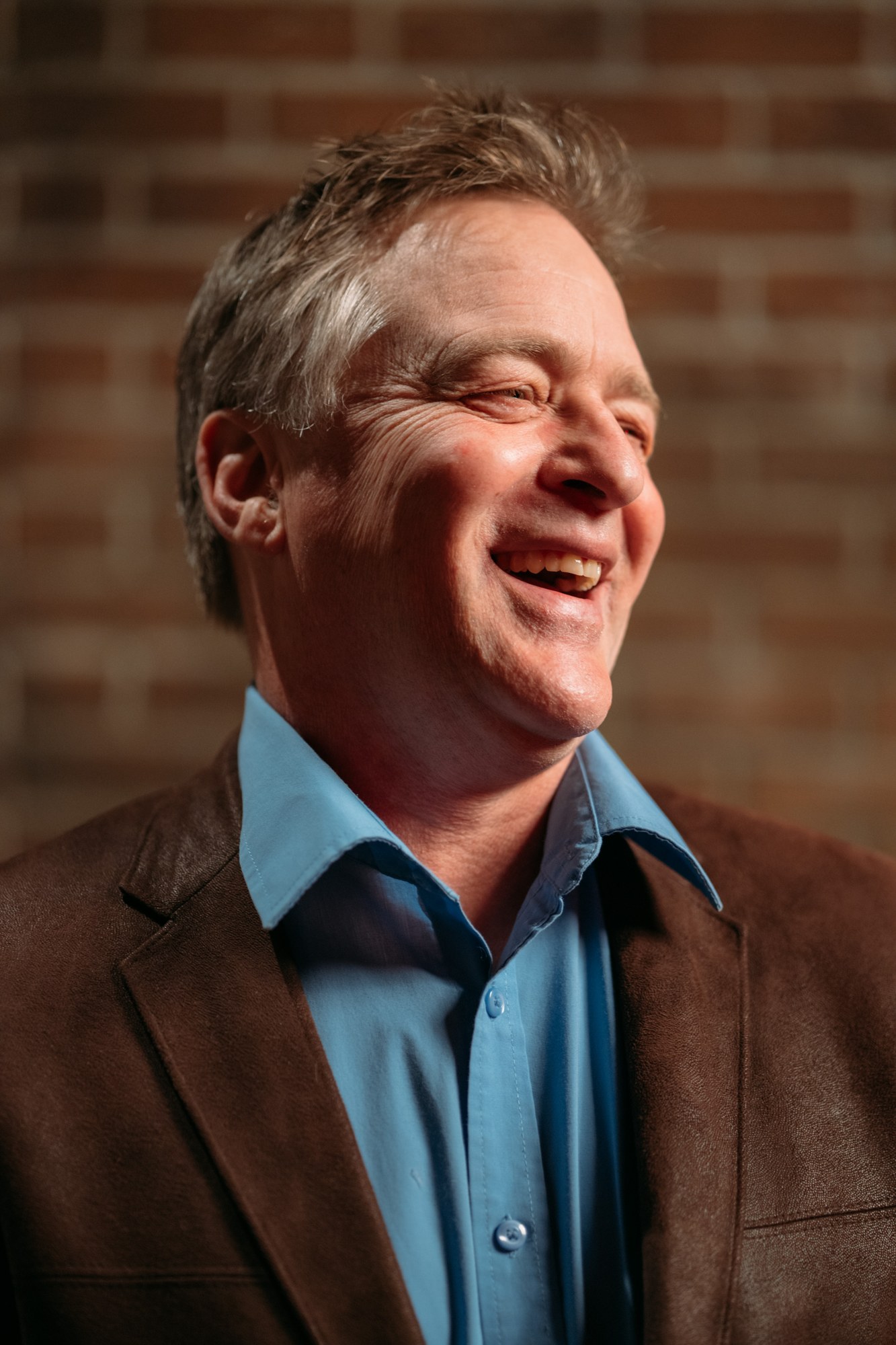 Roark Critchlow laughing in a blue shirt and brown jacket
