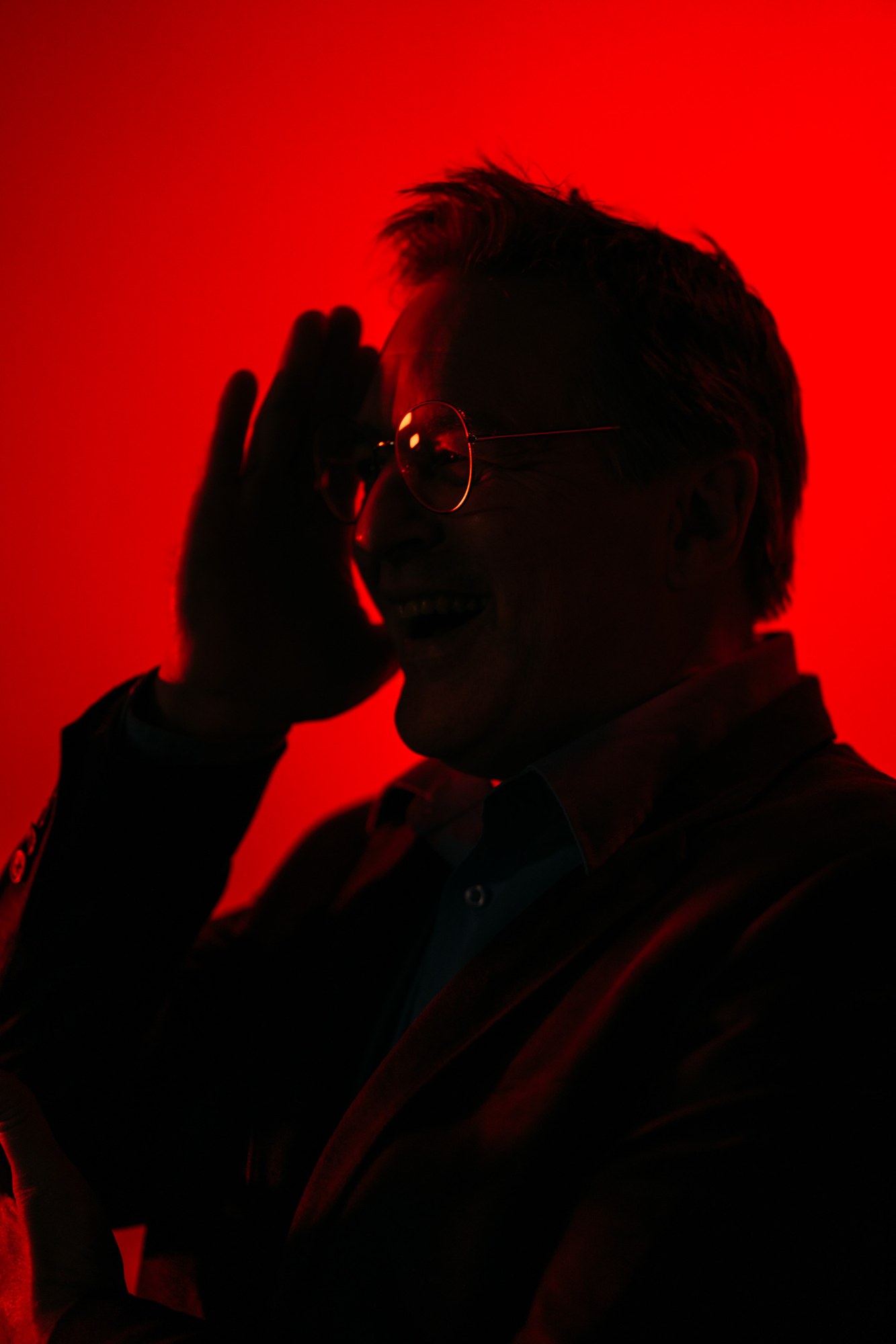 Roark adjusting his glasses under red studio light