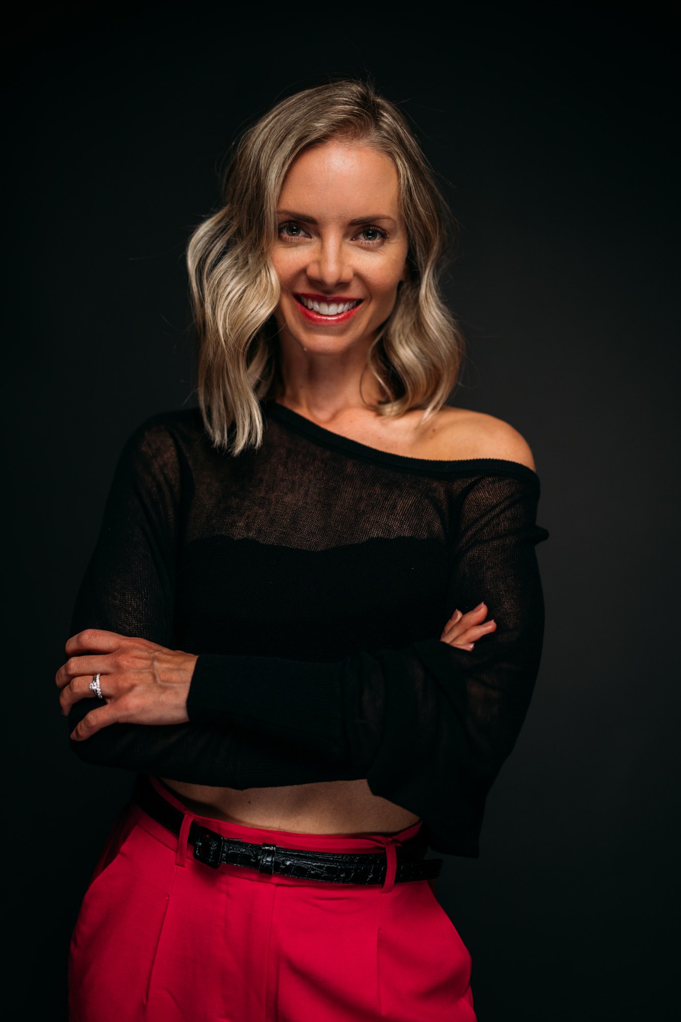 Sarah smiling in a black top and bright pink trousers