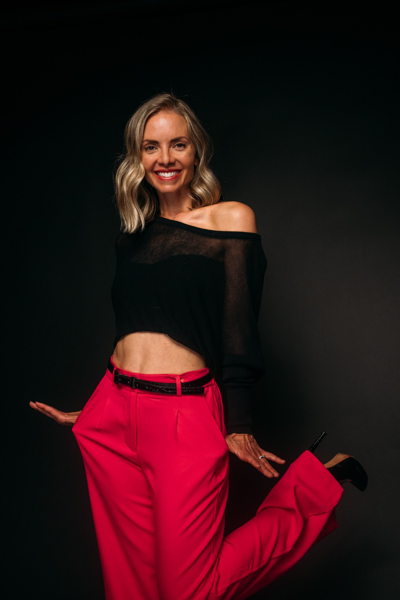 Sarah dancing in bright pink trousers against a black backdrop