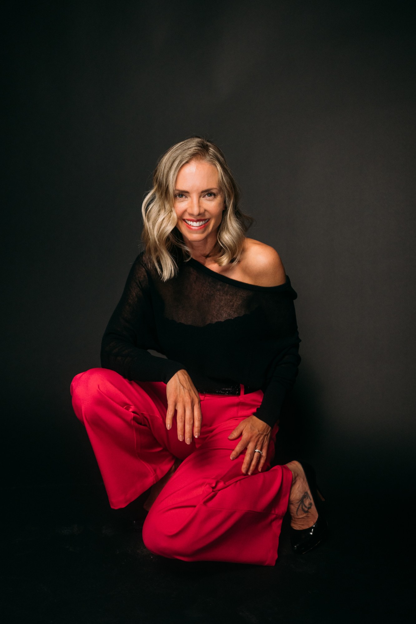 Sarah seated in pink trousers with her head tilted