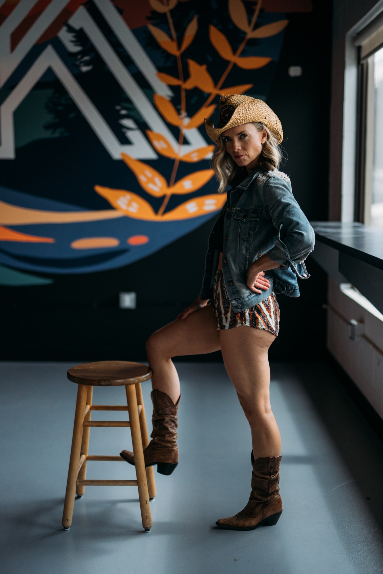 Sarah posing beside a stool in a denim jacket and cowboy hat