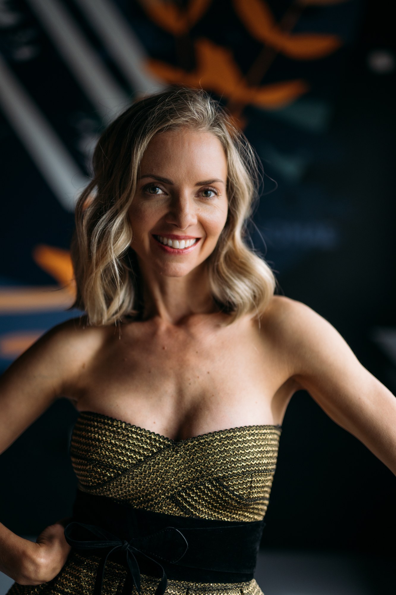 Sarah smiling in a gold dress beside the windows